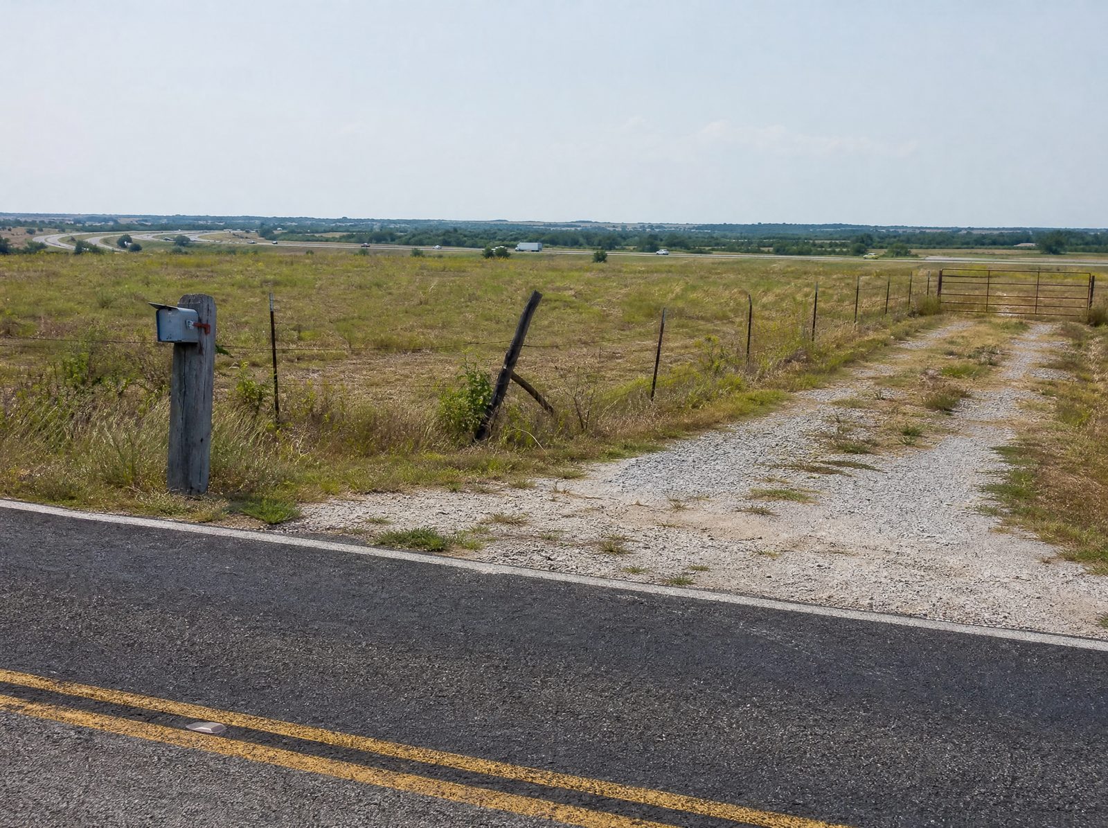 A Fort Bend County property with road frontage along a highway corridor, a gravel driveway and a wire fence line running toward the right-of-way