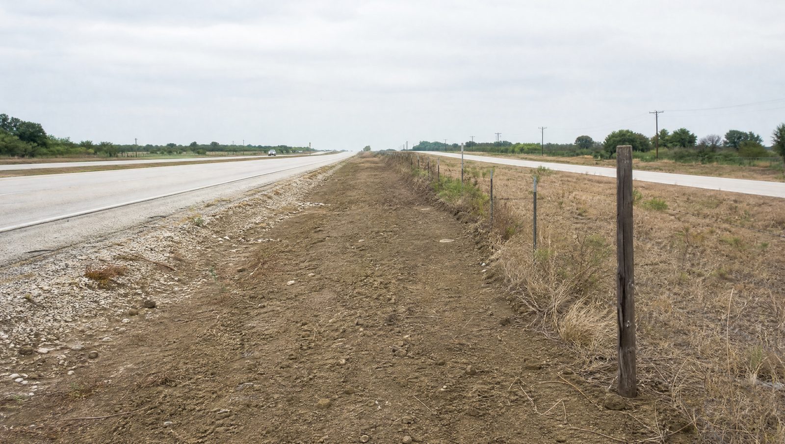 Ground level view of the SH 99 Grand Parkway right-of-way, a divided Texas highway with a wide graded corridor and a frontage road beside adjacent property
