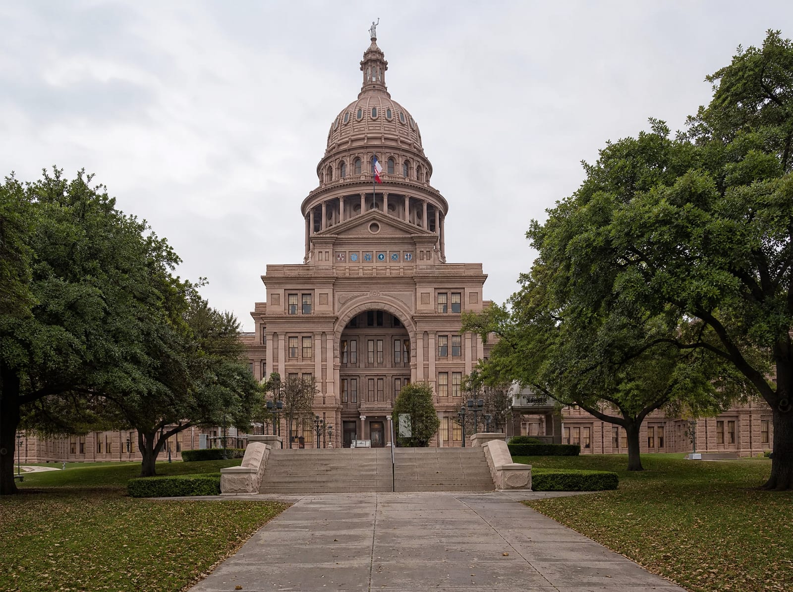 The Texas State Capitol building exterior in Austin, its domed limestone facade and grounds seen under even overcast daylight