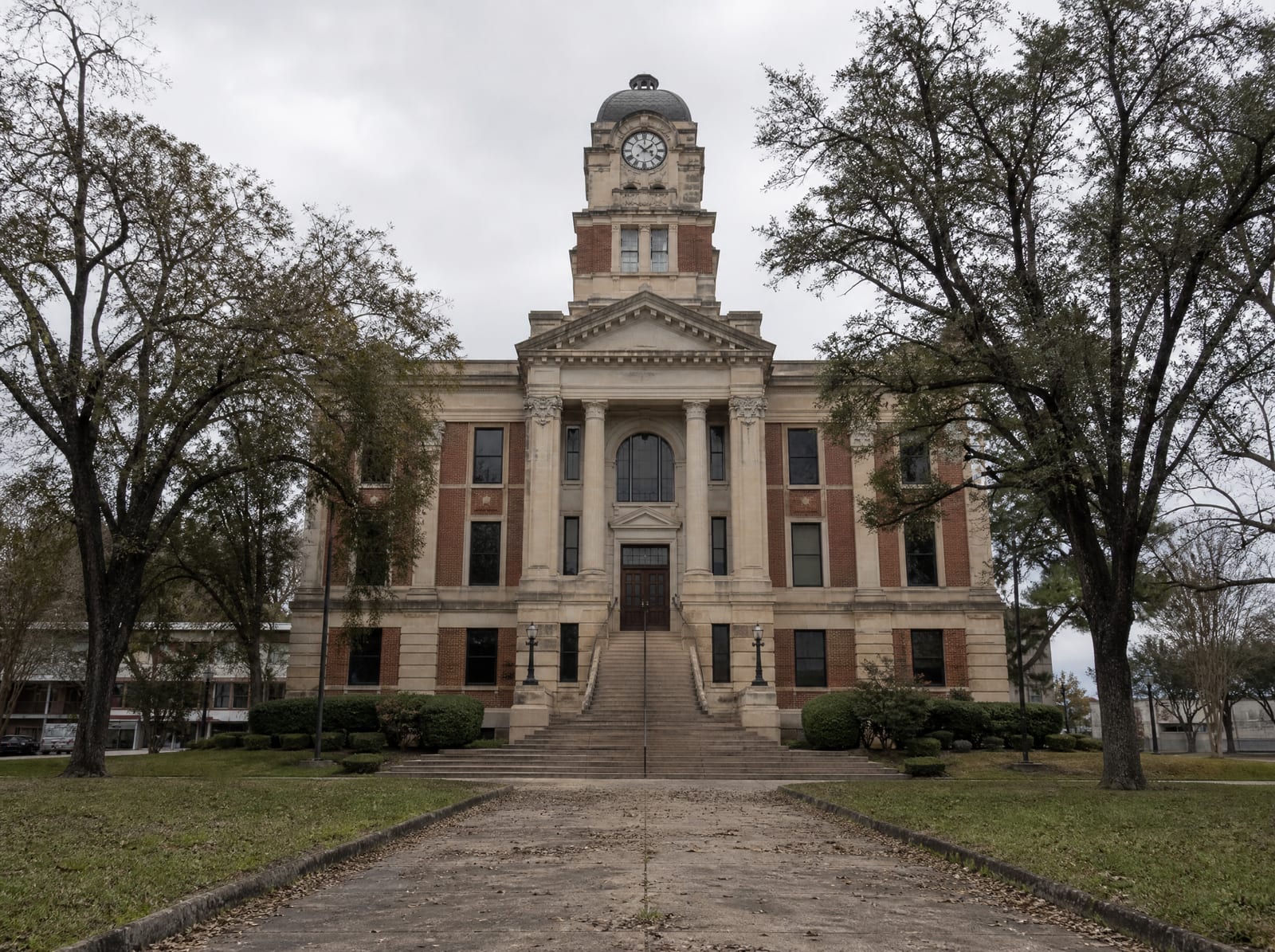 A Texas county courthouse building exterior under even daylight, a classic limestone and brick facade with a clock tower and landscaped grounds