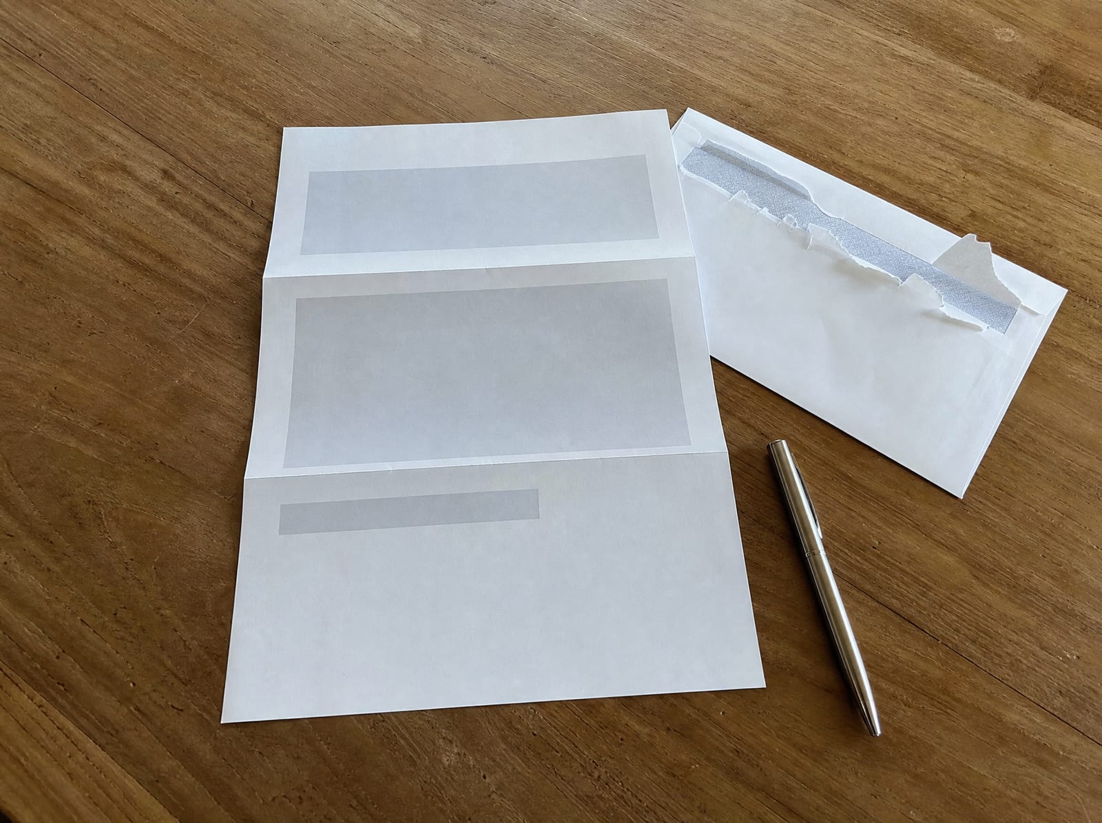 An opened official-looking letter and its envelope set out on a plain wooden table for review with no readable text