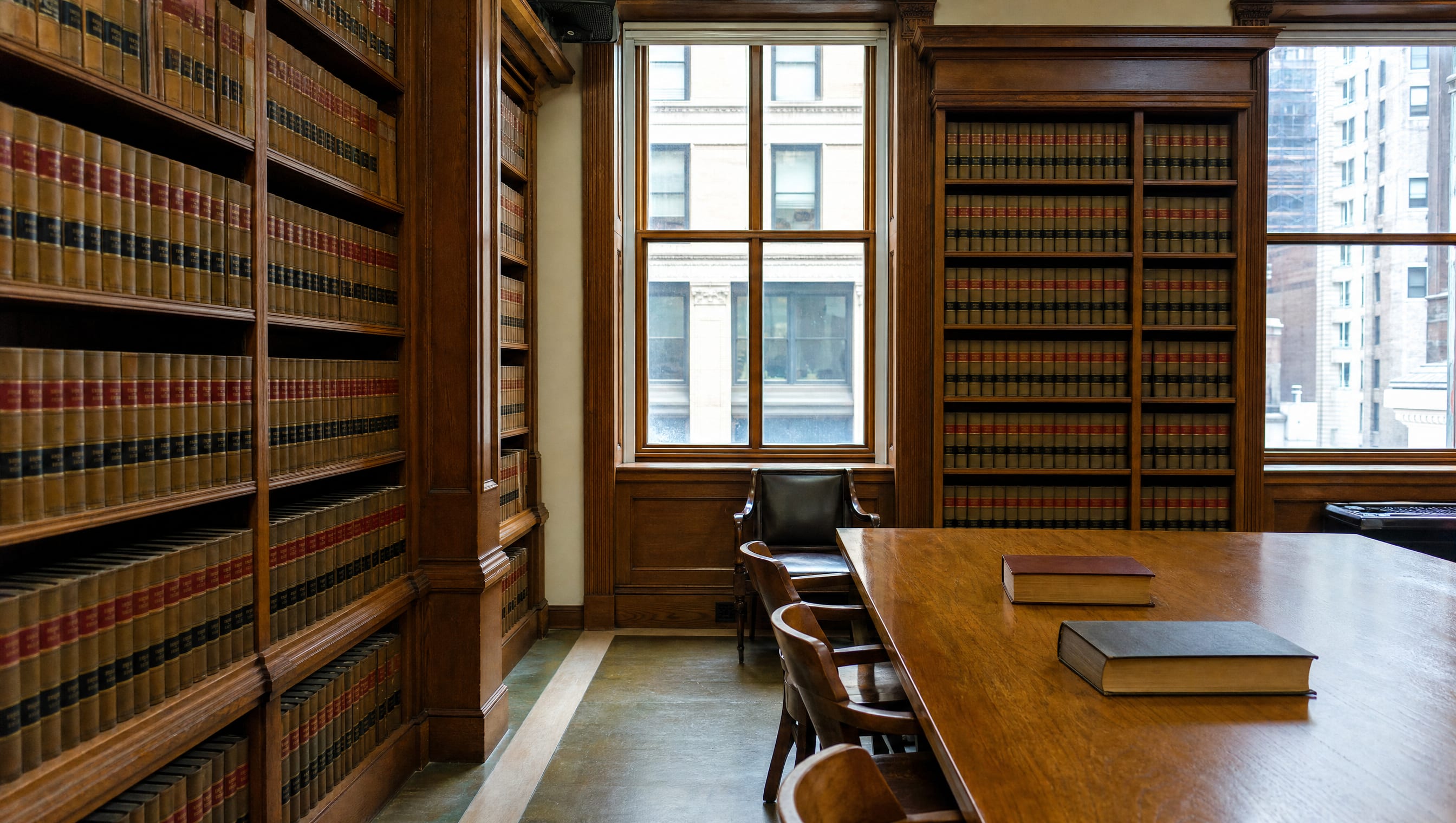 A bright law-firm library reading room with tall shelves of bound law reporters and a long reading table under soft daylight
