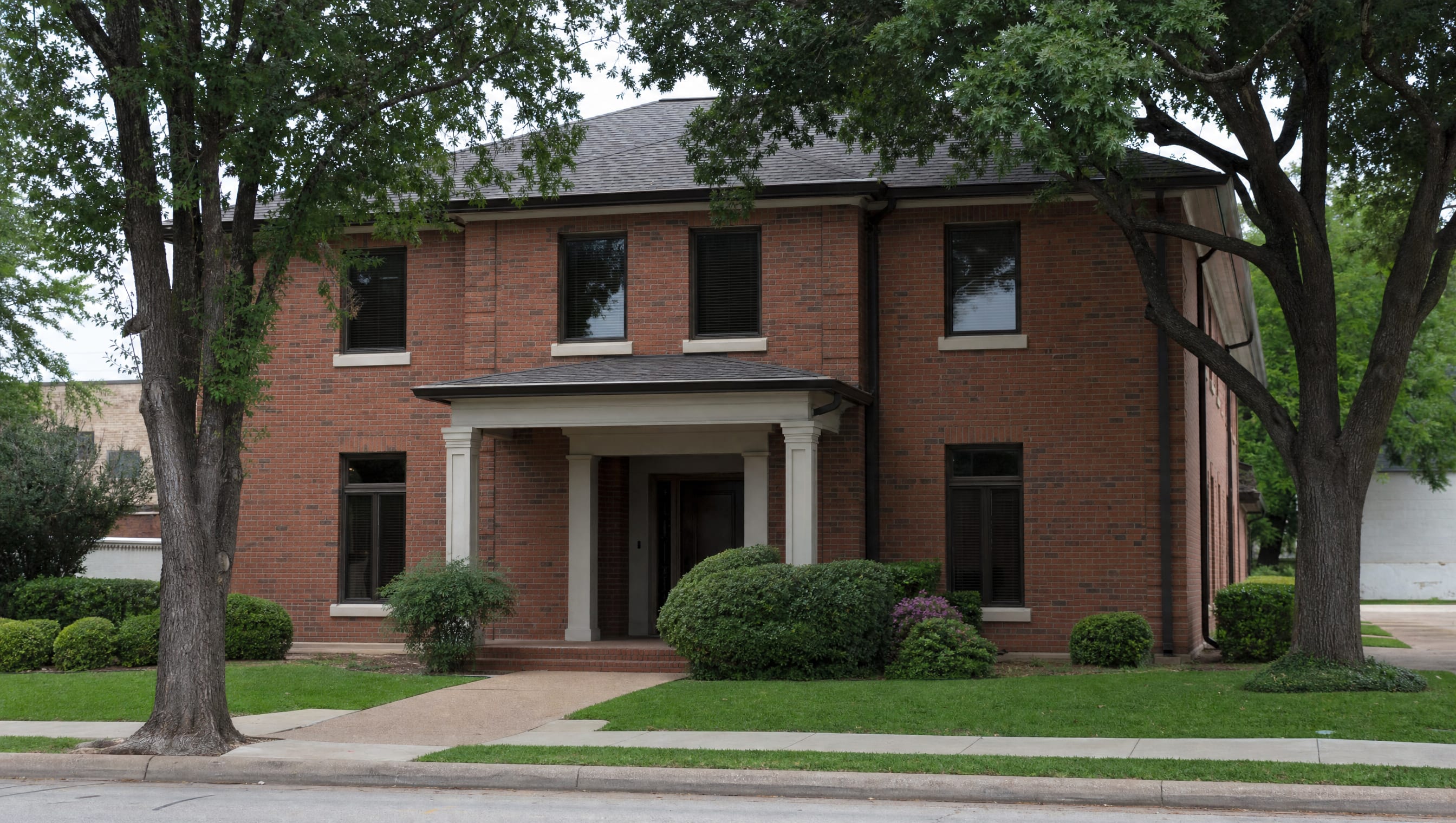 A dignified two-story red-brick professional law-office building with a covered entrance and mature landscaping in a small Texas town