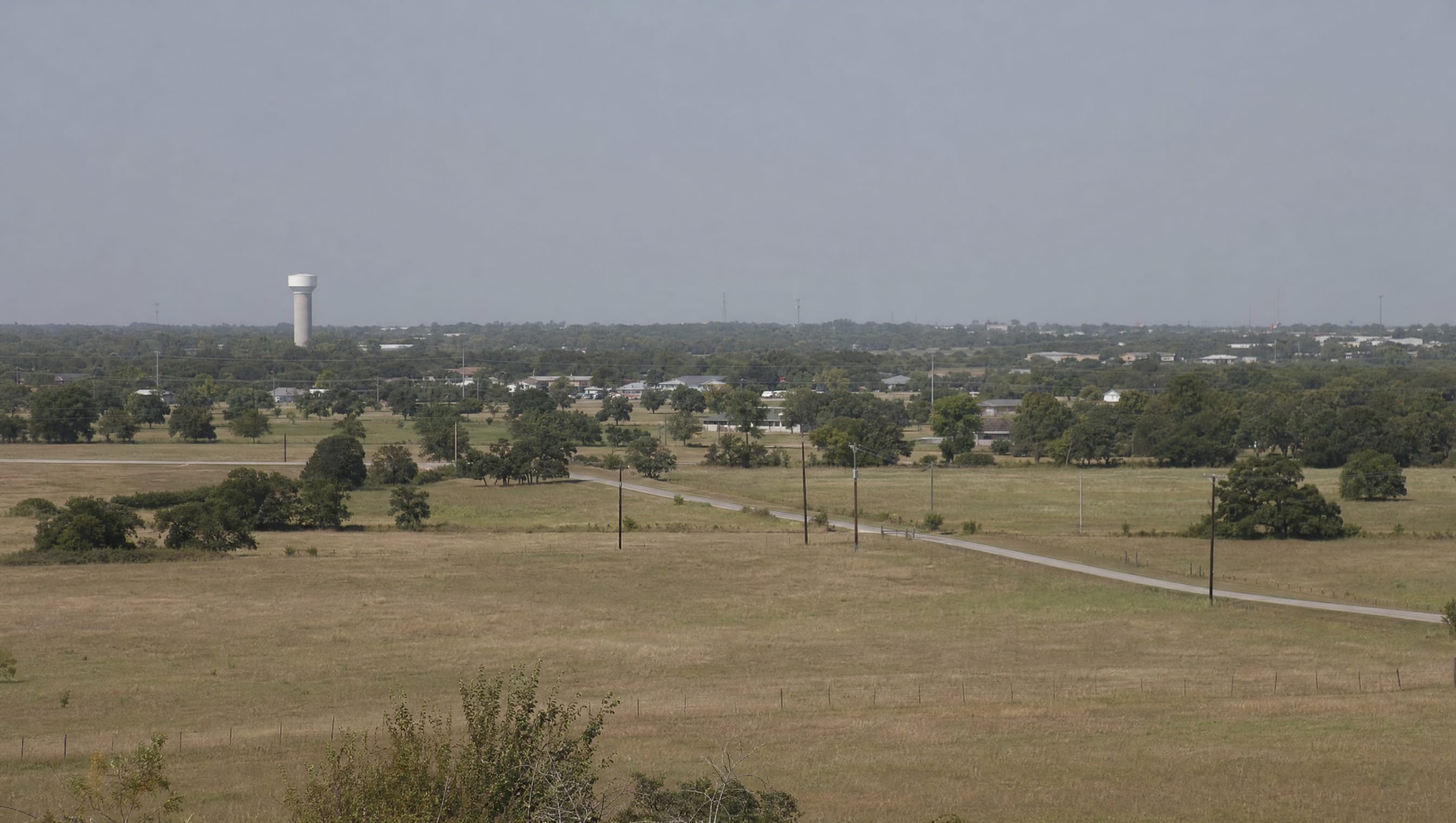 The flat Greater Houston and Fort Bend County coastal plain of fields and live oaks with a small-town water tower and rooftops on the horizon