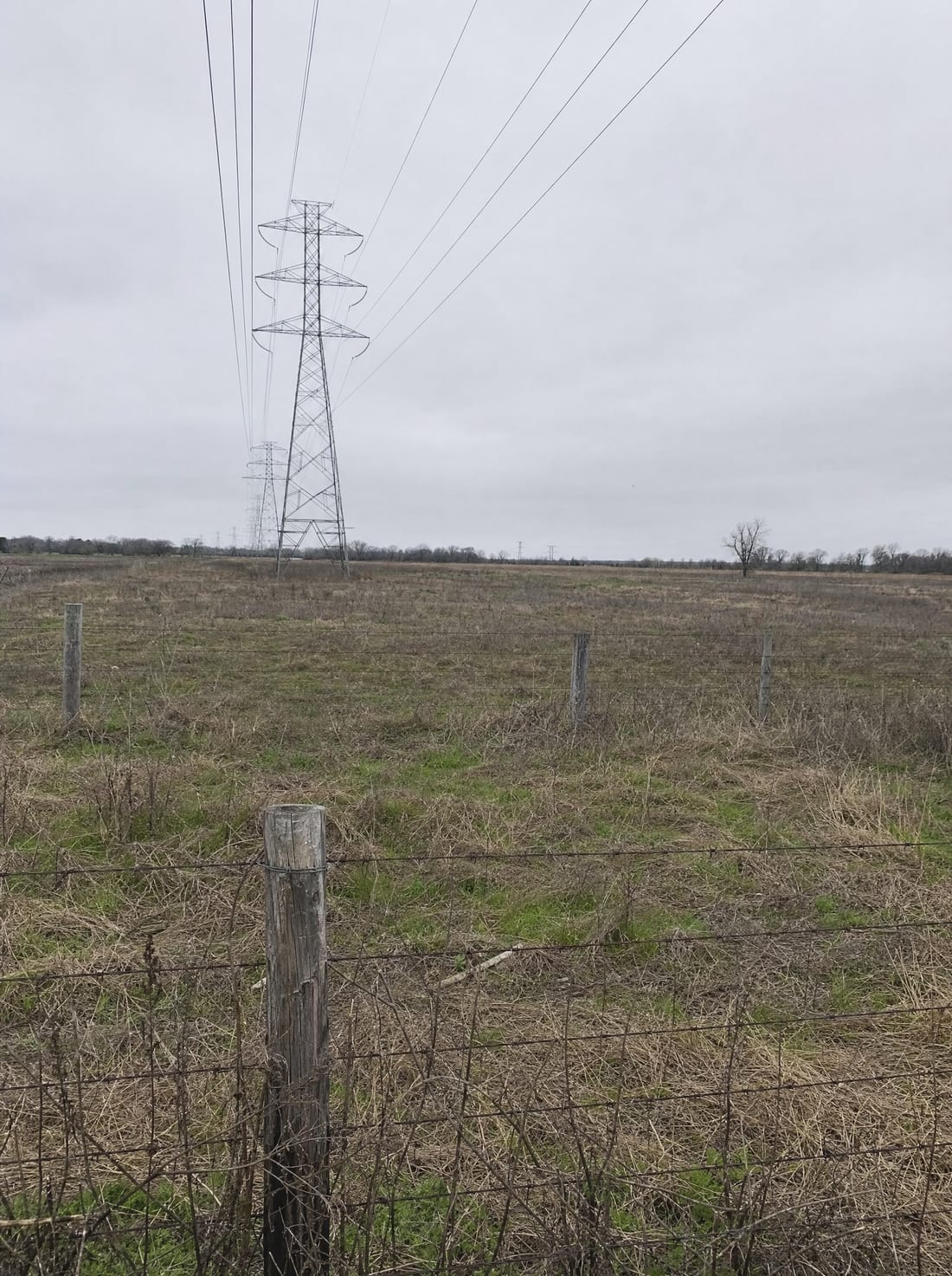 A rural Texas parcel with tall transmission towers and power lines crossing a right-of-way and a barbed-wire fence, facing condemnation for infrastructure