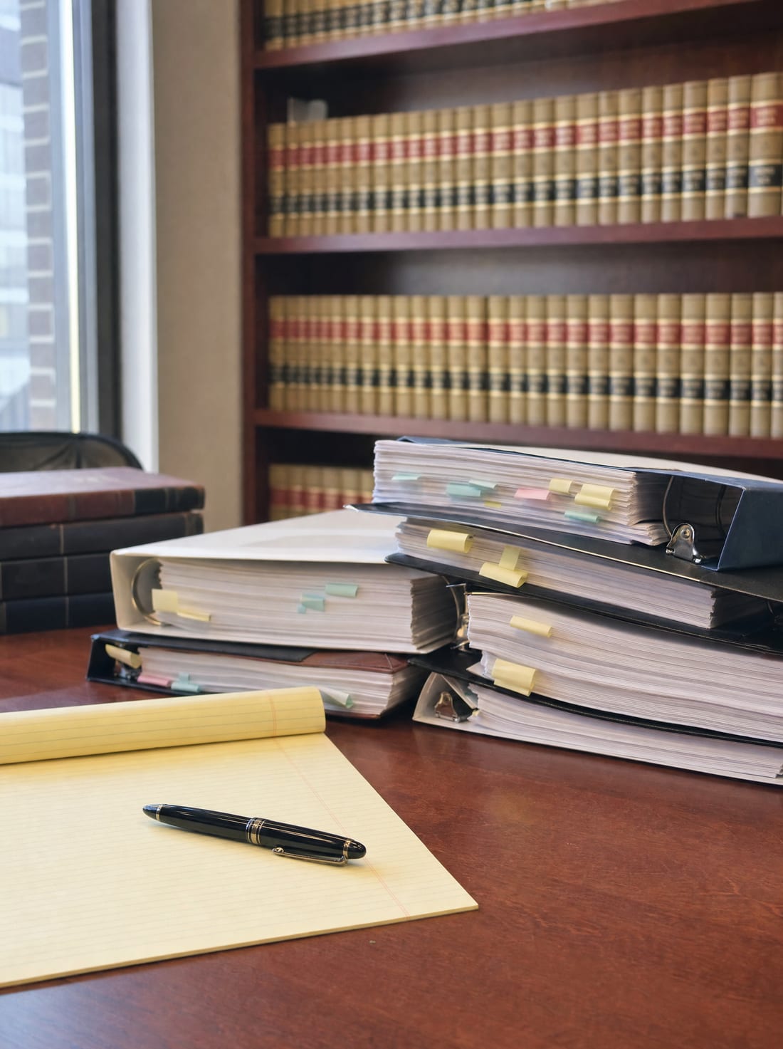 A table stacked with tabbed exhibit binders and a legal pad, for trial preparation and litigation