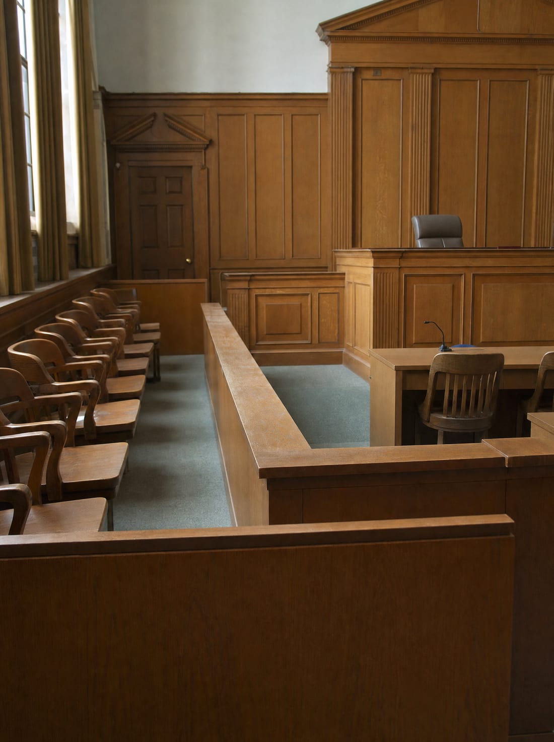 An empty courtroom with a wooden jury box and a judge's bench in soft daylight, for a jury trial
