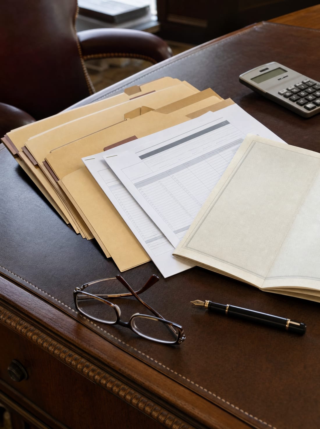 An organized desk with property deeds, brokerage and retirement statements, and a policy folder laid out for a full review of a family's holdings