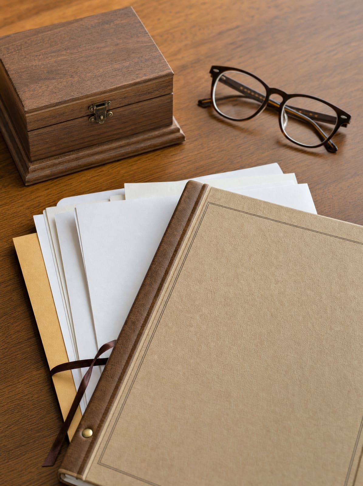 A bound will and estate documents, a small wooden keepsake box, and reading glasses on a warm wood desk, representing an estate or probate conflict suited for mediation