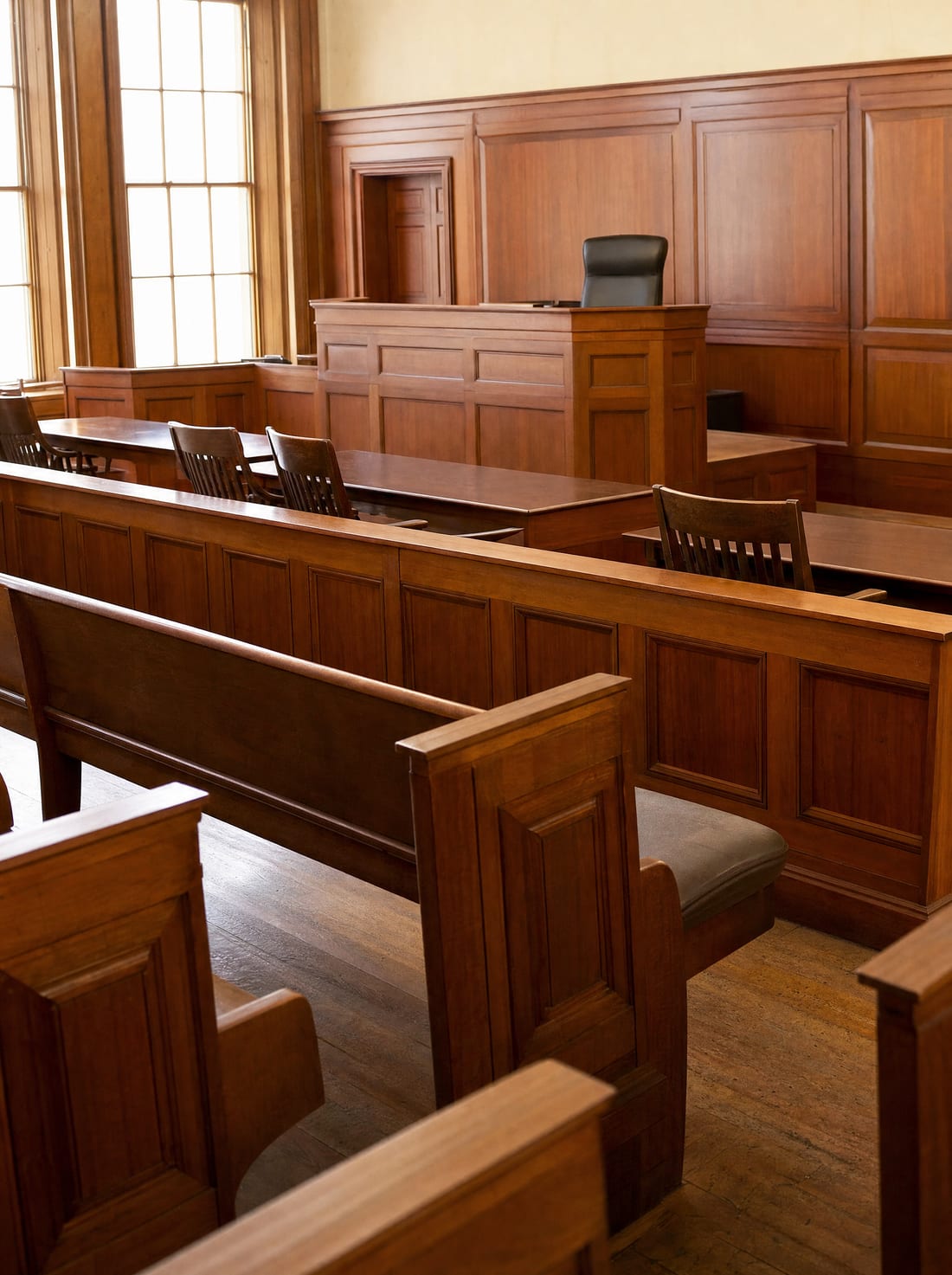 A quiet empty wood-paneled county courtroom with benches, a judge's bench, and counsel tables in soft daylight