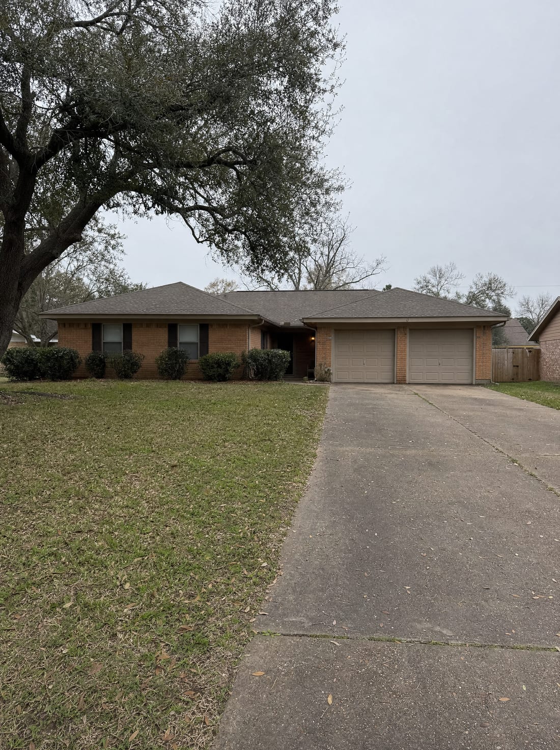 A modest single-story Texas brick home with a lawn and a live oak under an overcast sky, an ordinary property being appraised