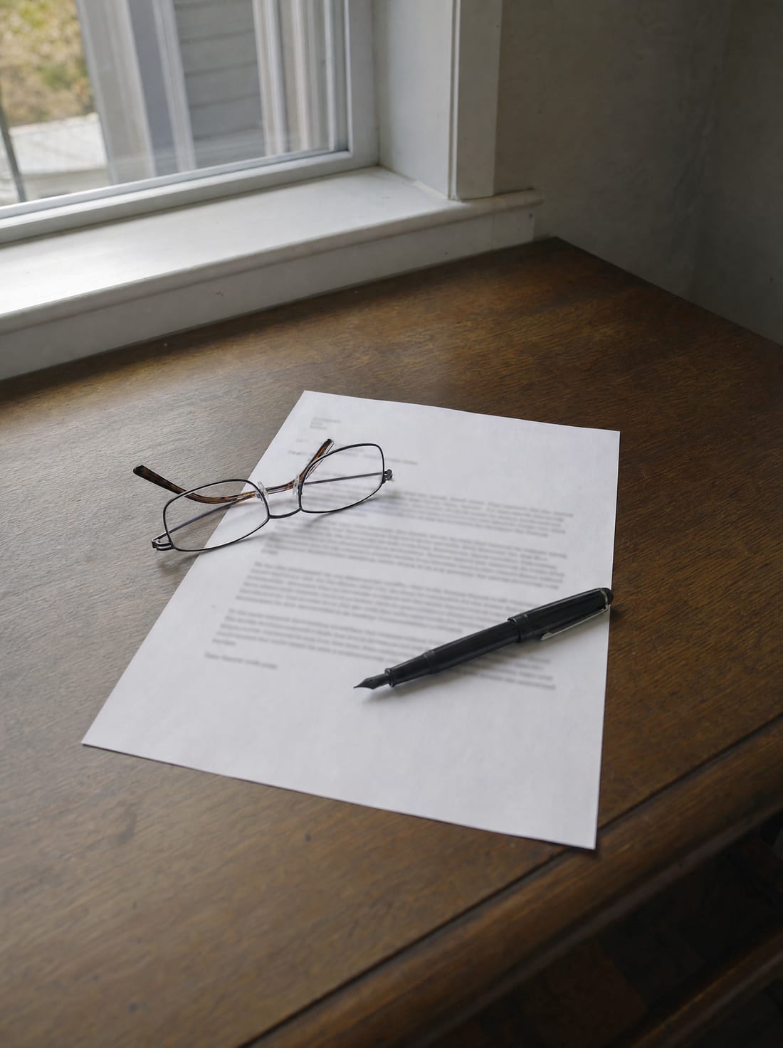 A desk by a window with a condemnation offer letter, reading glasses, and a pen, for reviewing the initial offer