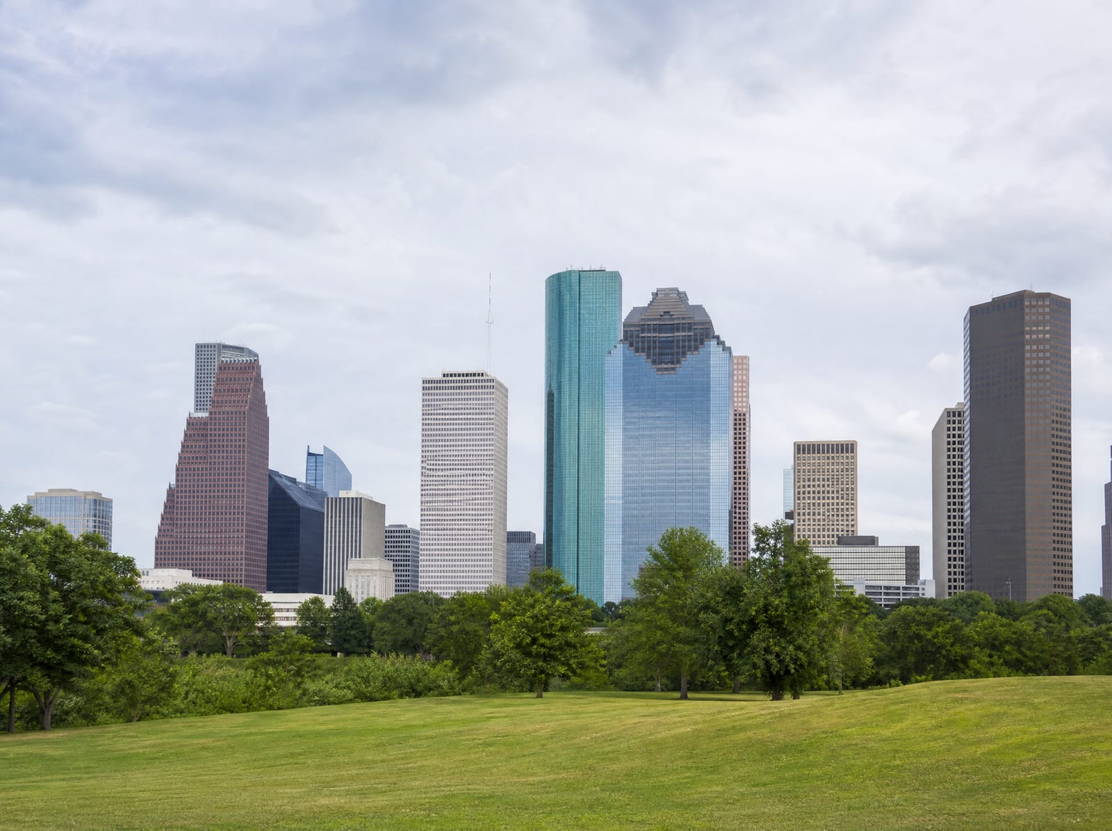 The Greater Houston business district skyline of modern office towers seen across open green space under a soft sky, representing businesses served throughout the region