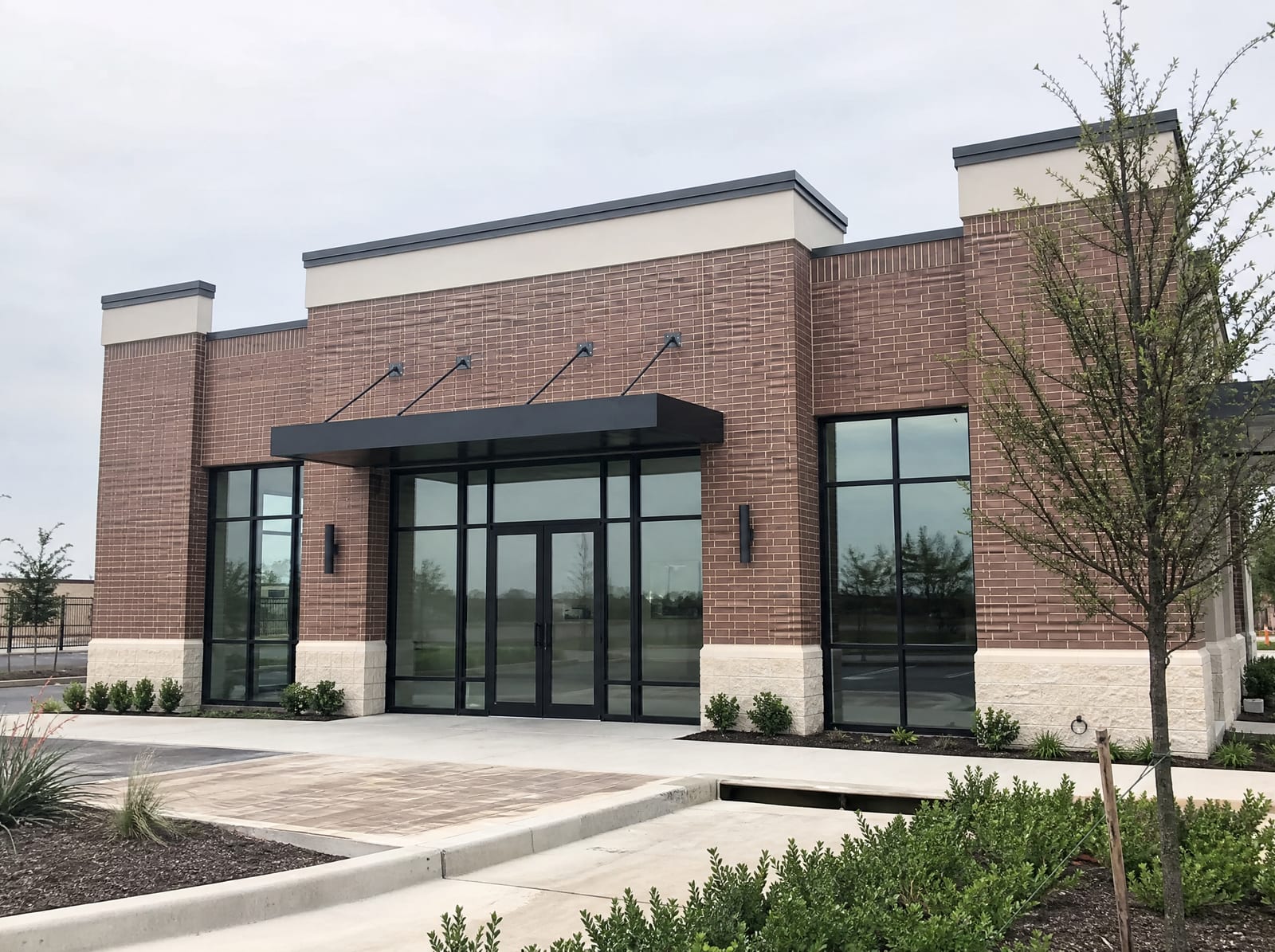 A clean, modern small commercial building or storefront for a new Texas business, with a brick and glass facade and tidy landscaping