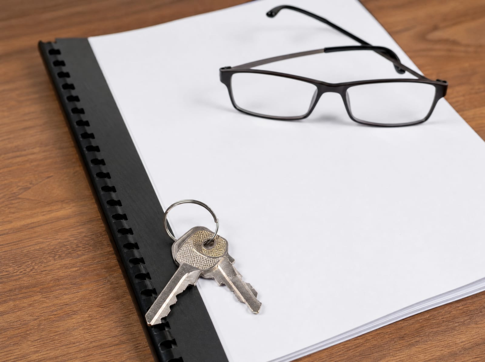 A close view of a bound commercial lease agreement on a warm wood desk with a set of keys and reading glasses, representing a commercial lease and real estate transaction