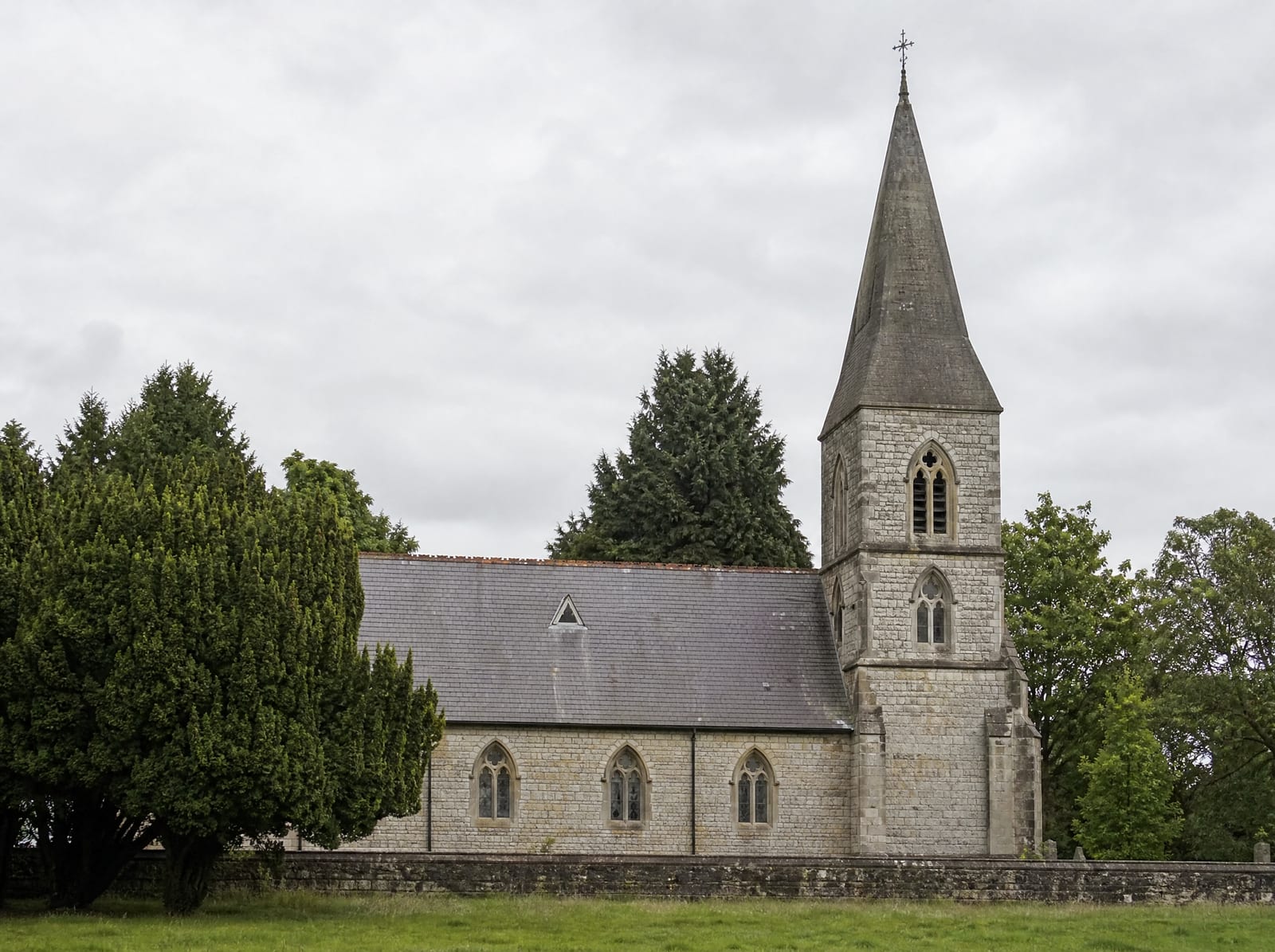 A traditional stone church building with a steeple and arched windows, seen calmly at a respectful distance among mature trees under a soft sky, representing the institutions held accountable