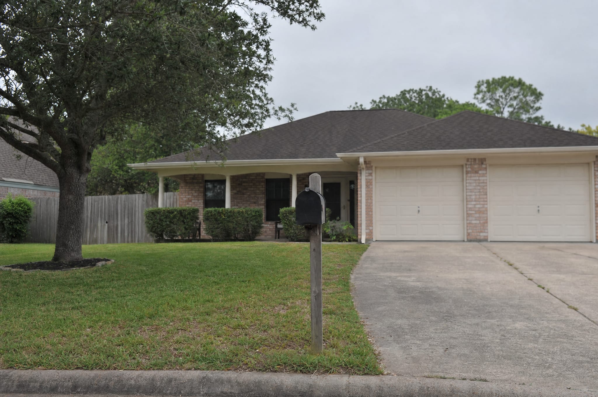 A modest single-story Texas ranch-style home with a covered front porch, a mown lawn, and a driveway under a soft overcast sky