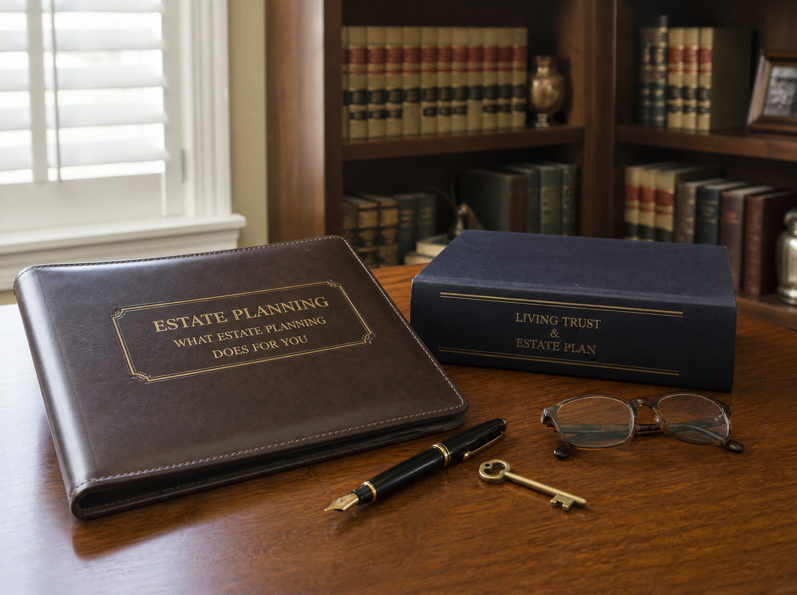 An estate-planning document folder and a bound trust binder on a warm wood desk with a fountain pen, reading glasses, and a small brass key