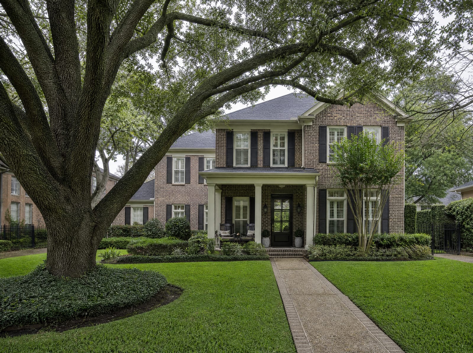 A welcoming established two-story brick Texas family home with a covered porch, manicured lawn, and a mature live oak, the legacy an estate plan protects