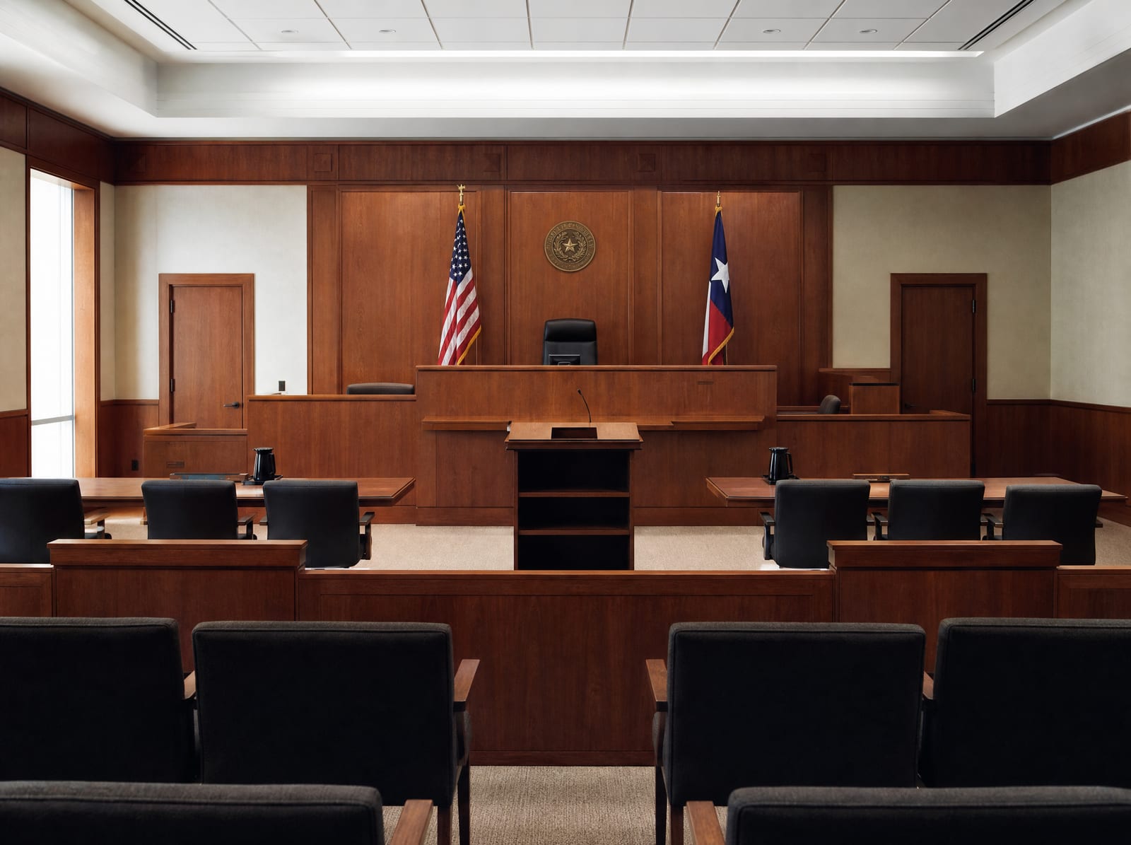 An orderly courtroom with a judge's bench, a witness stand, counsel tables, and flags, for motion practice and pre-trial proceedings