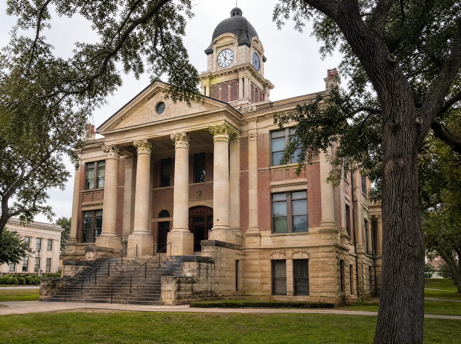 A dignified historic Texas county courthouse of limestone and red brick with a clock tower and columns among live oaks, where injury cases are tried