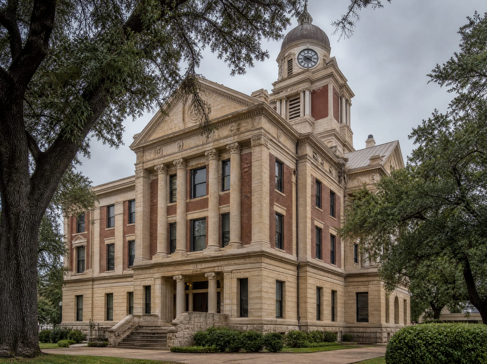 A dignified historic Texas county courthouse of limestone and red brick with a clock tower and columns among live oaks, where probate matters and will-validity disputes are heard