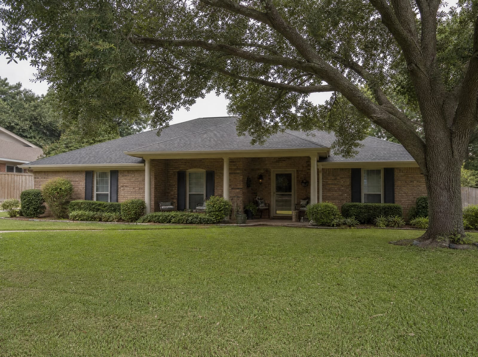 A warm, established single-story brick Texas family home with a covered porch, a mown lawn, and mature shade trees, the family property passing to heirs through probate
