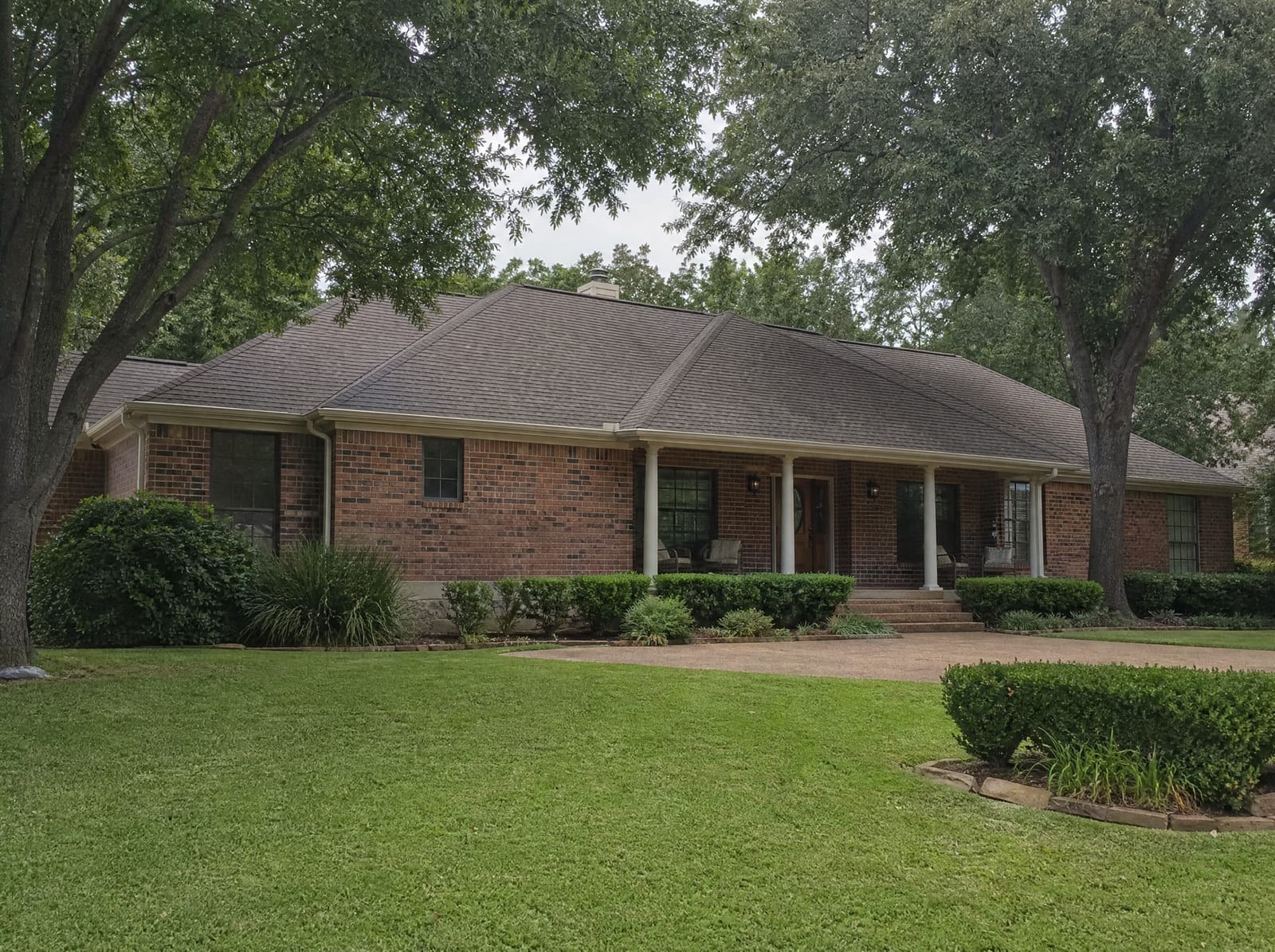 A well-kept established brick Texas home with a covered porch, a mown lawn, and mature shade trees, a residential property interest