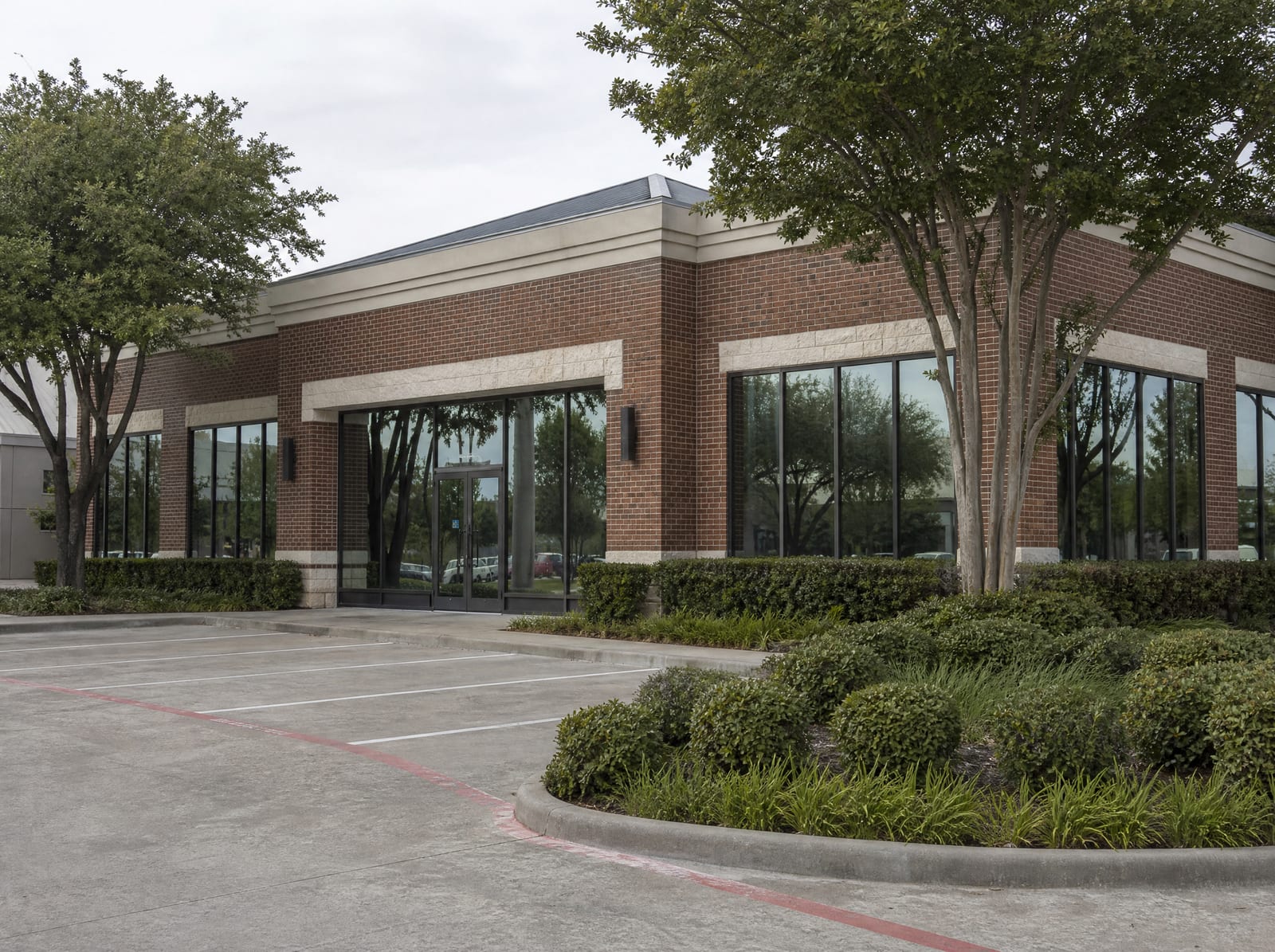 A well-kept single-story brick and glass Texas commercial office or retail building with a clean parking lot and tidy landscaping