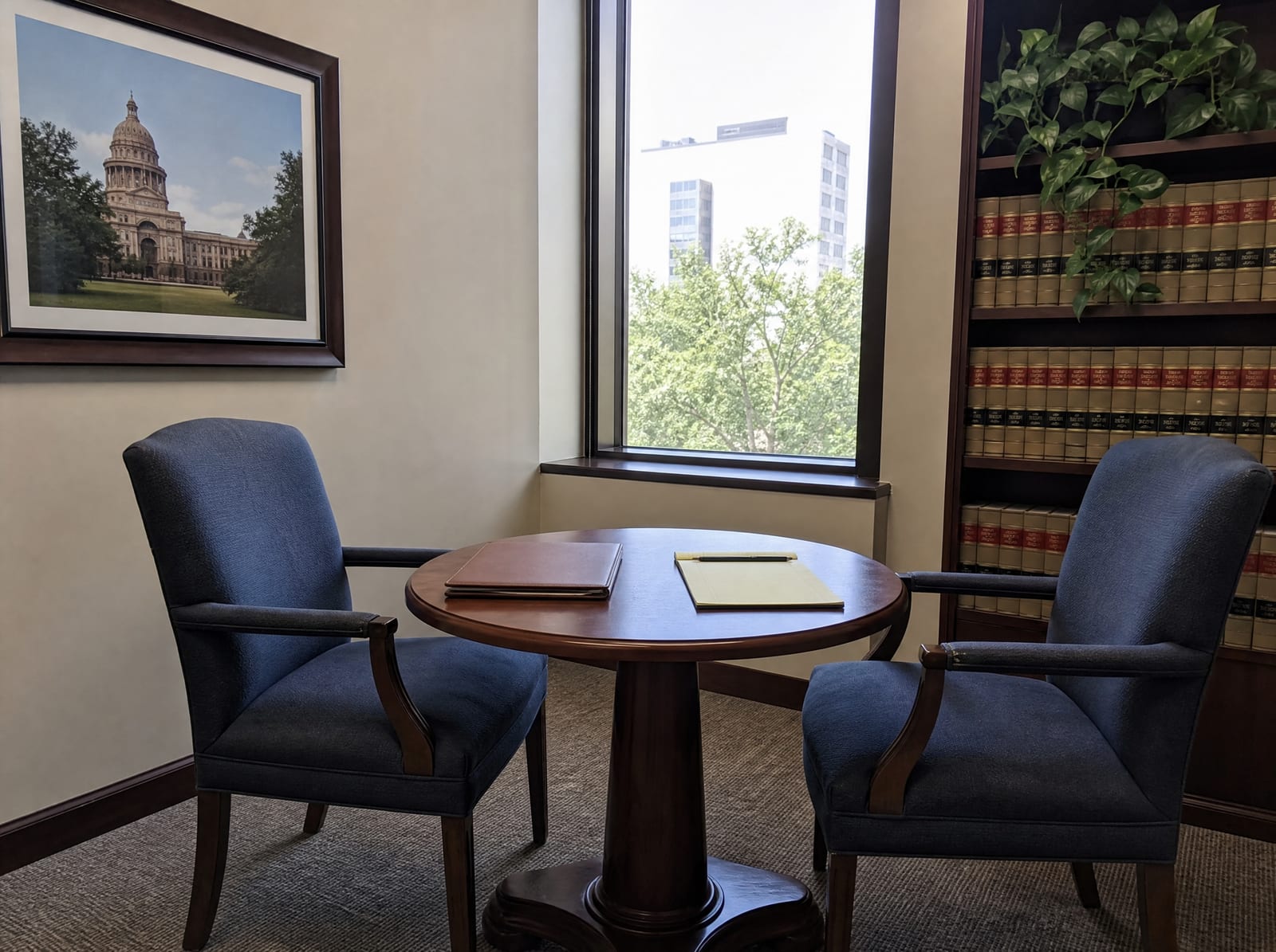 A calm law-office consultation corner with two chairs, a small table, law books, and a plant by a window