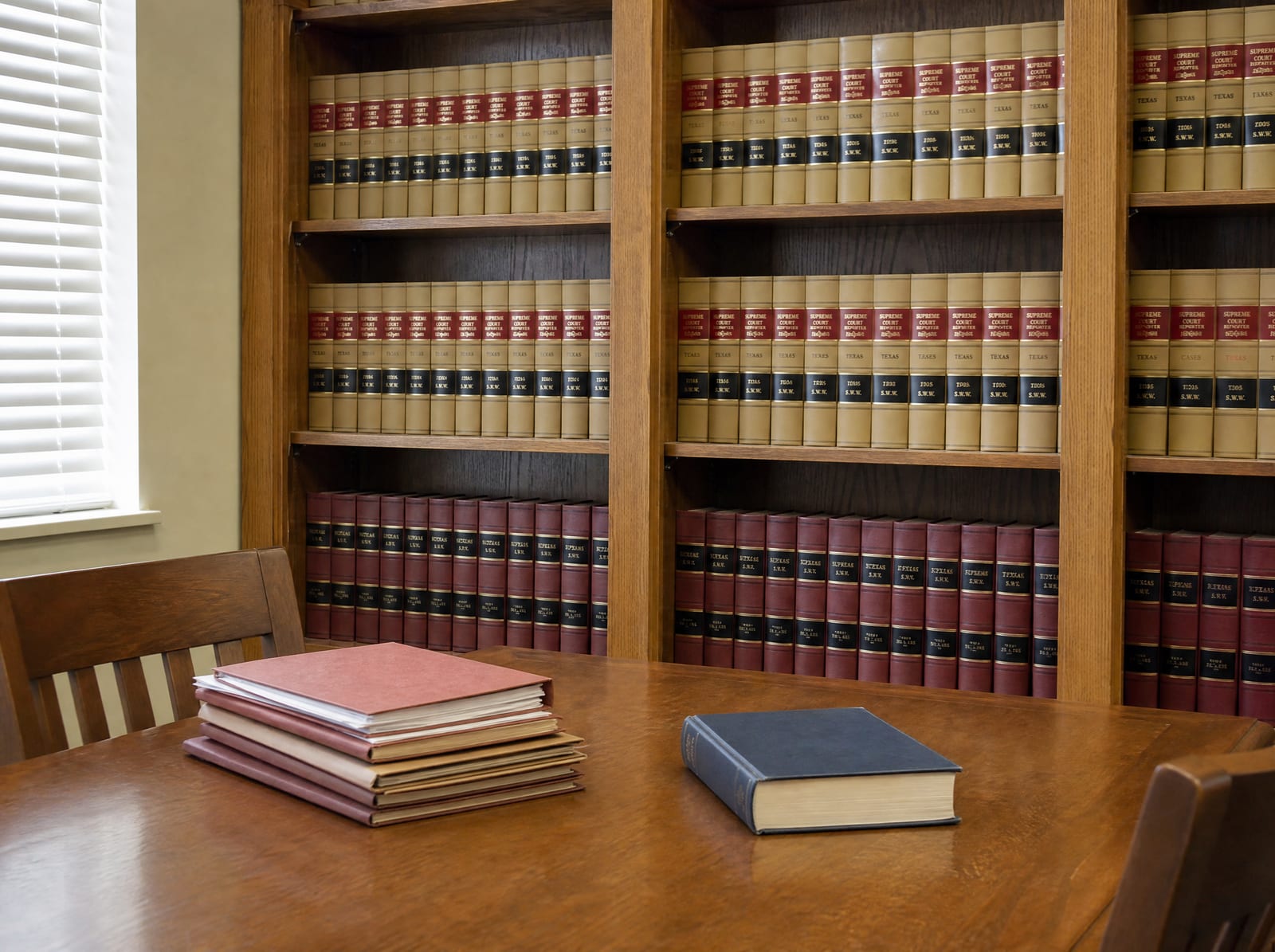 A law-firm library shelf of bound law reporters beside a reading table with a neat stack of closed case files