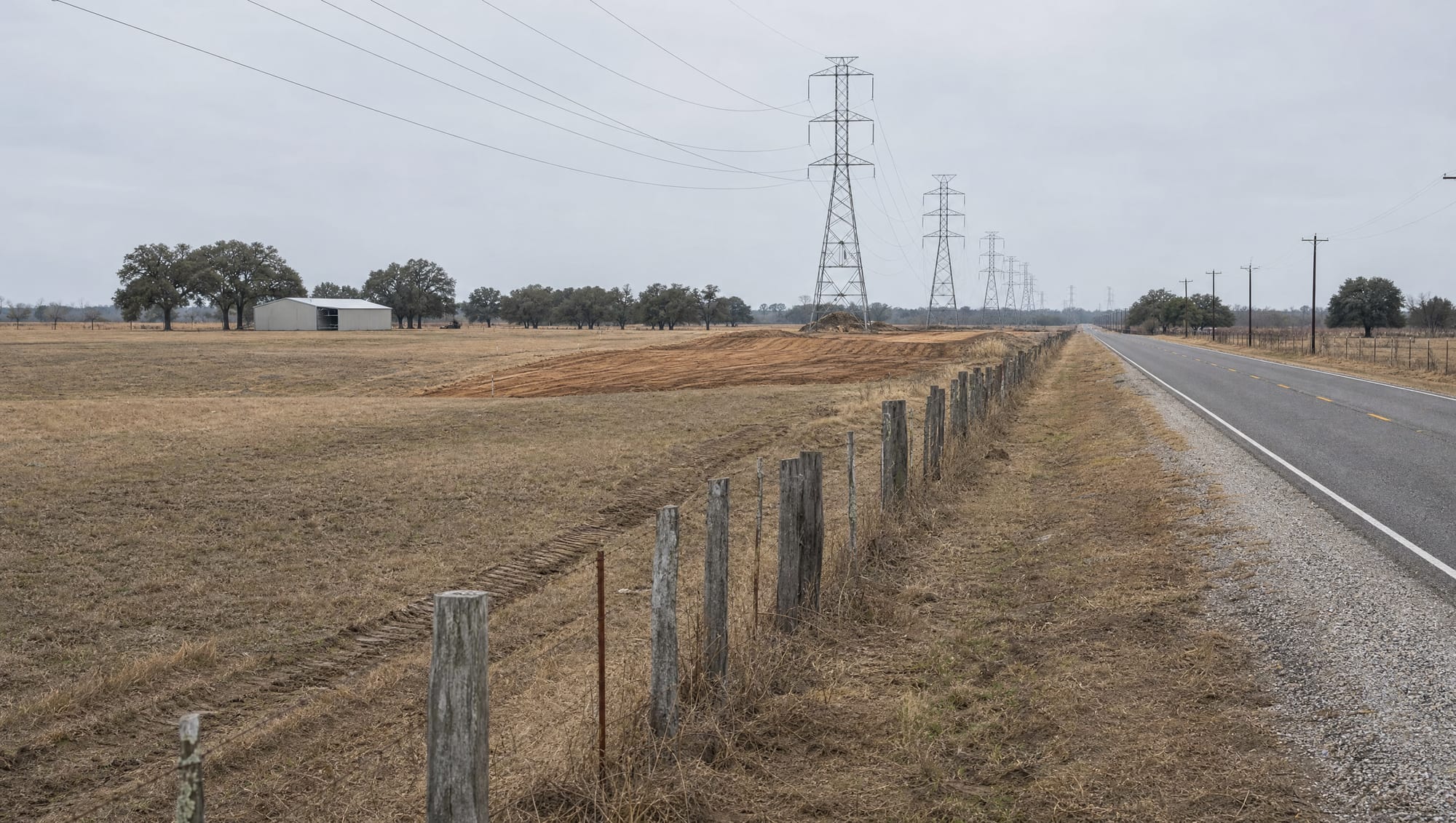 A rural Fort Bend County, Texas landowner's fenced pastureland along a two-lane county road, with electric transmission towers and a freshly graded right-of-way cut crossing the property under an overcast sky