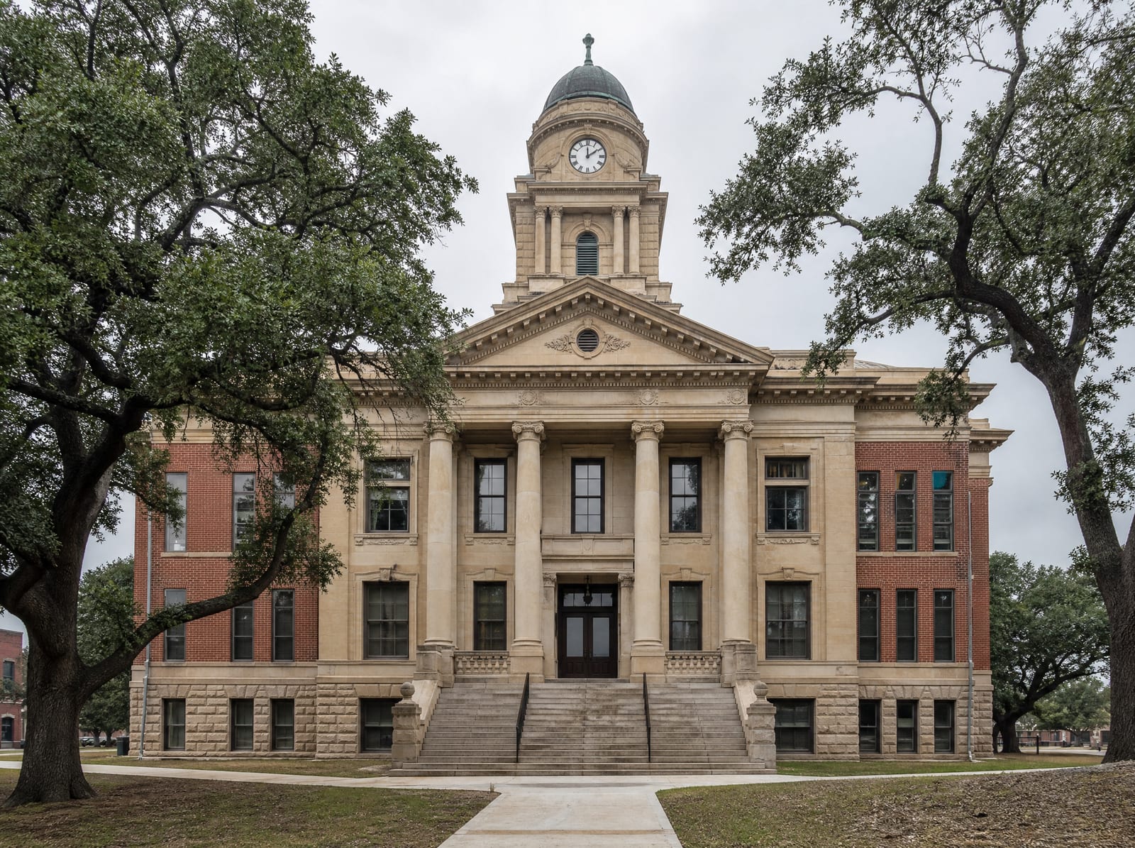 A historic limestone and brick Texas county courthouse with a clock tower and columns among live oaks, where compensation challenges are heard