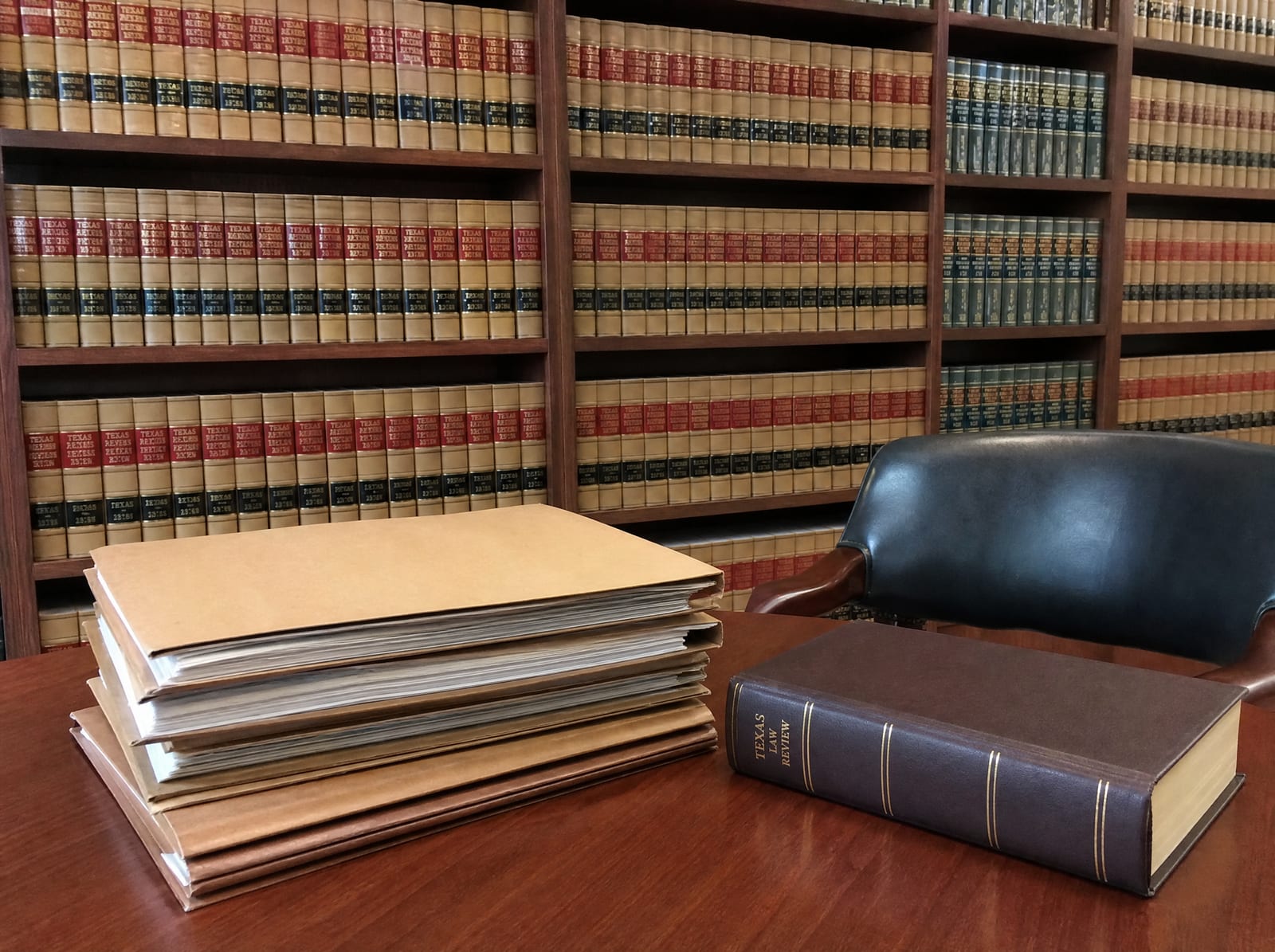 A law-firm library wall of bound law reporters beside a reading table with a neat stack of closed case files