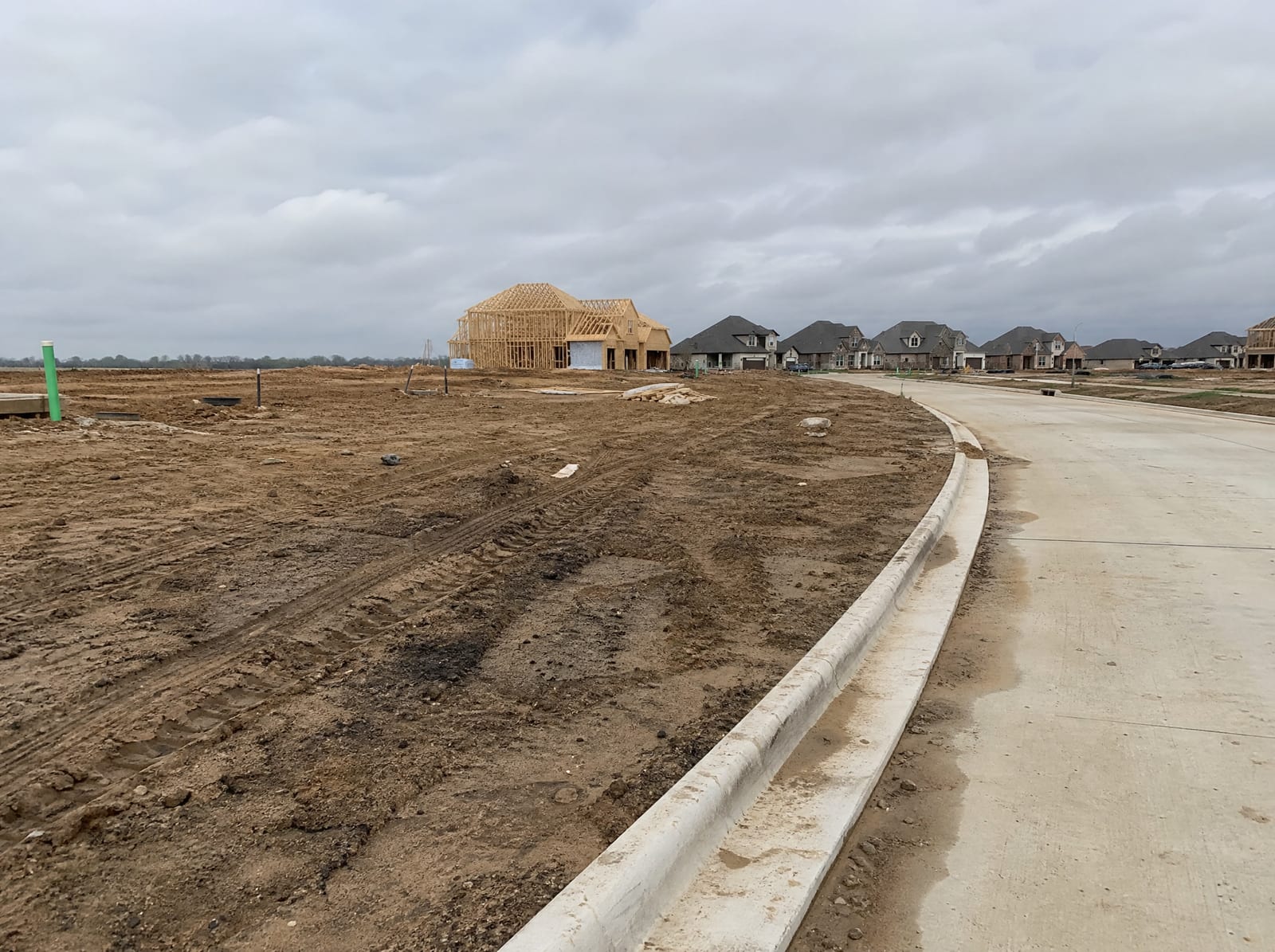 A newer subdivision under development near Fulshear, Texas, with freshly graded lots, new concrete curbs and streets, homes under construction, and open cleared ranch land transitioning into master-planned suburbia