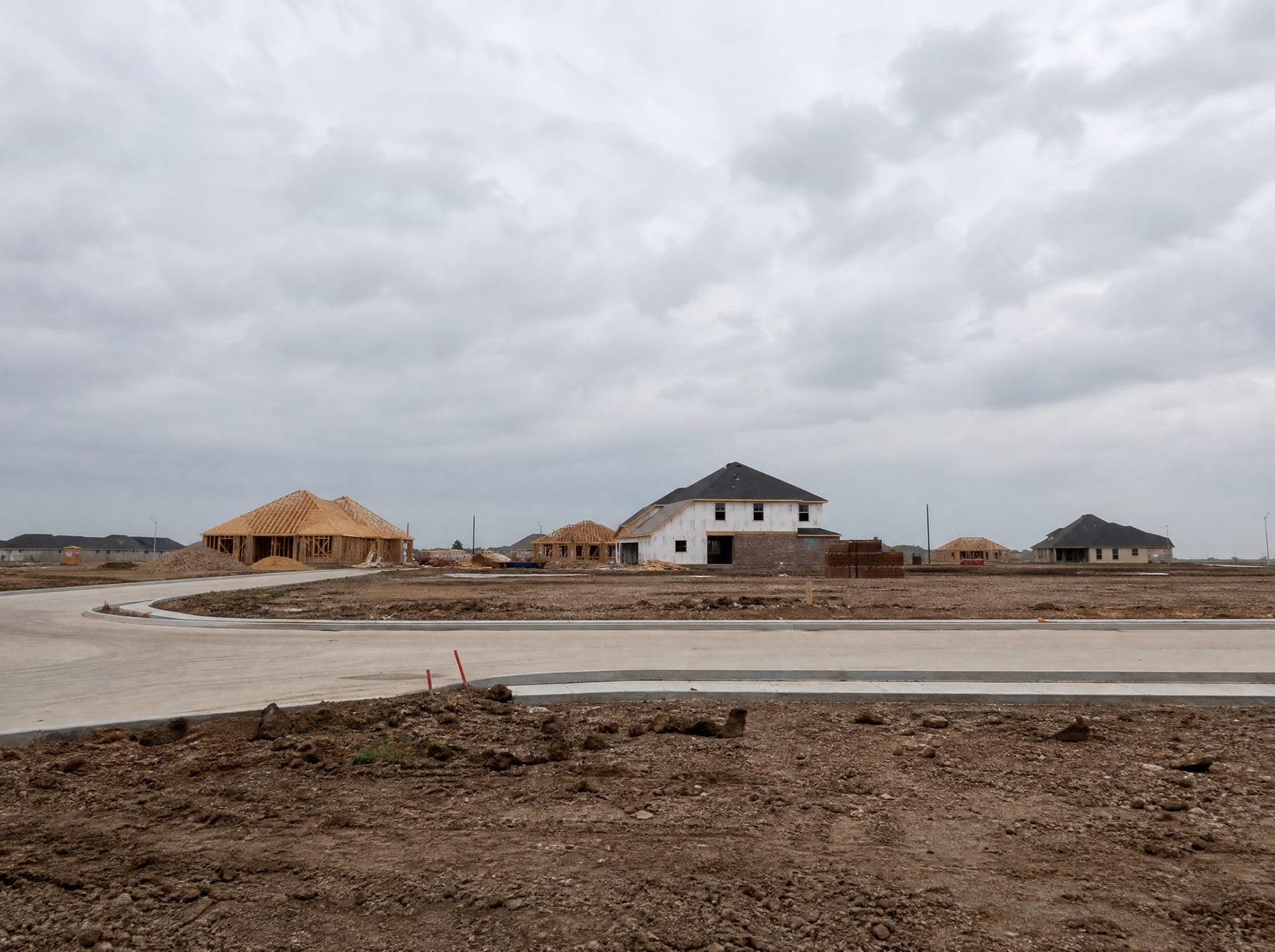 A newer subdivision under development in Pearland, Texas, with freshly graded lots, new concrete curbs and streets, homes under construction, and open cleared Brazoria County land transitioning into suburbia