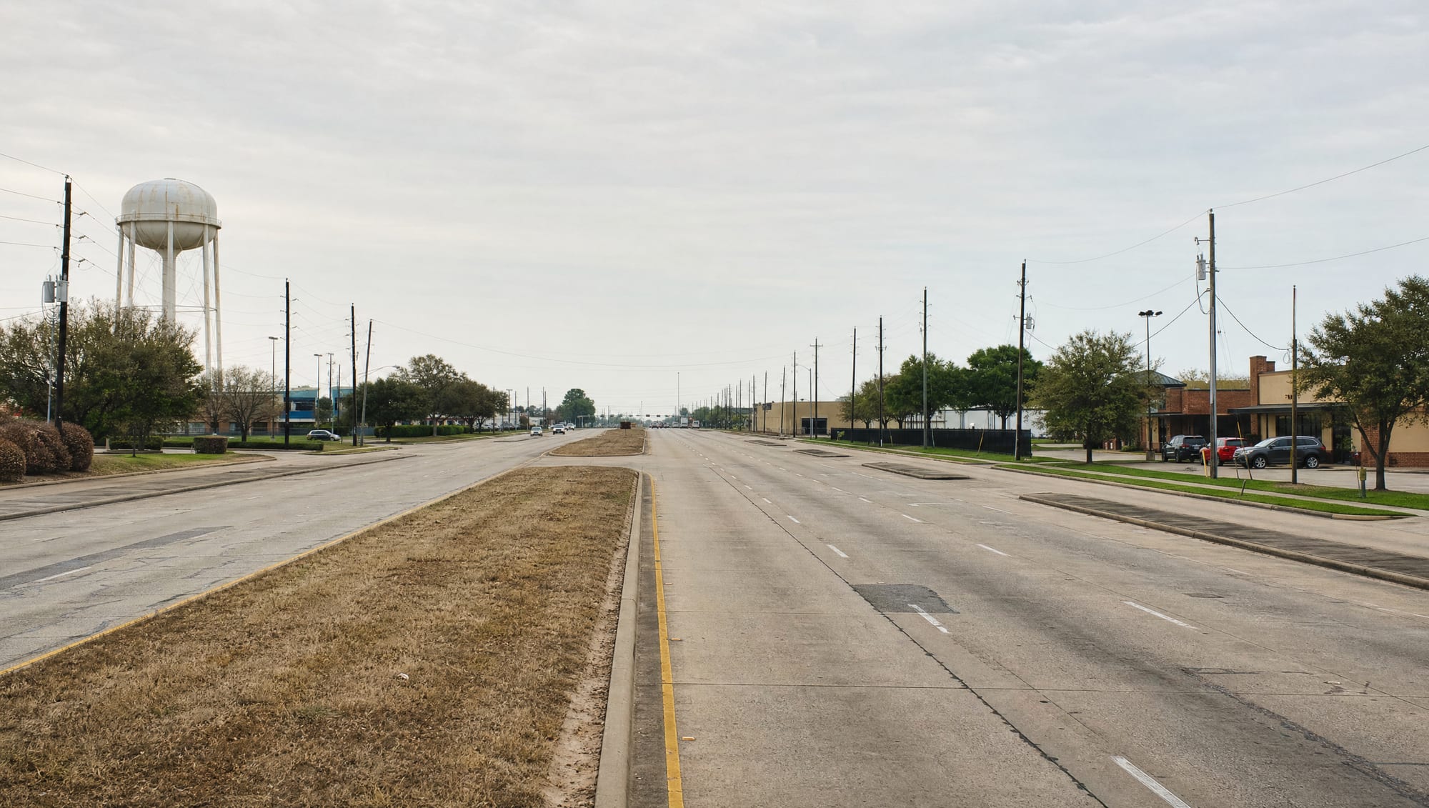 A wide divided US-59 and State Highway 36 commercial corridor running through Rosenberg, Texas in Fort Bend County, with small-city commercial frontage, a water tower, and utility lines under a big pale sky