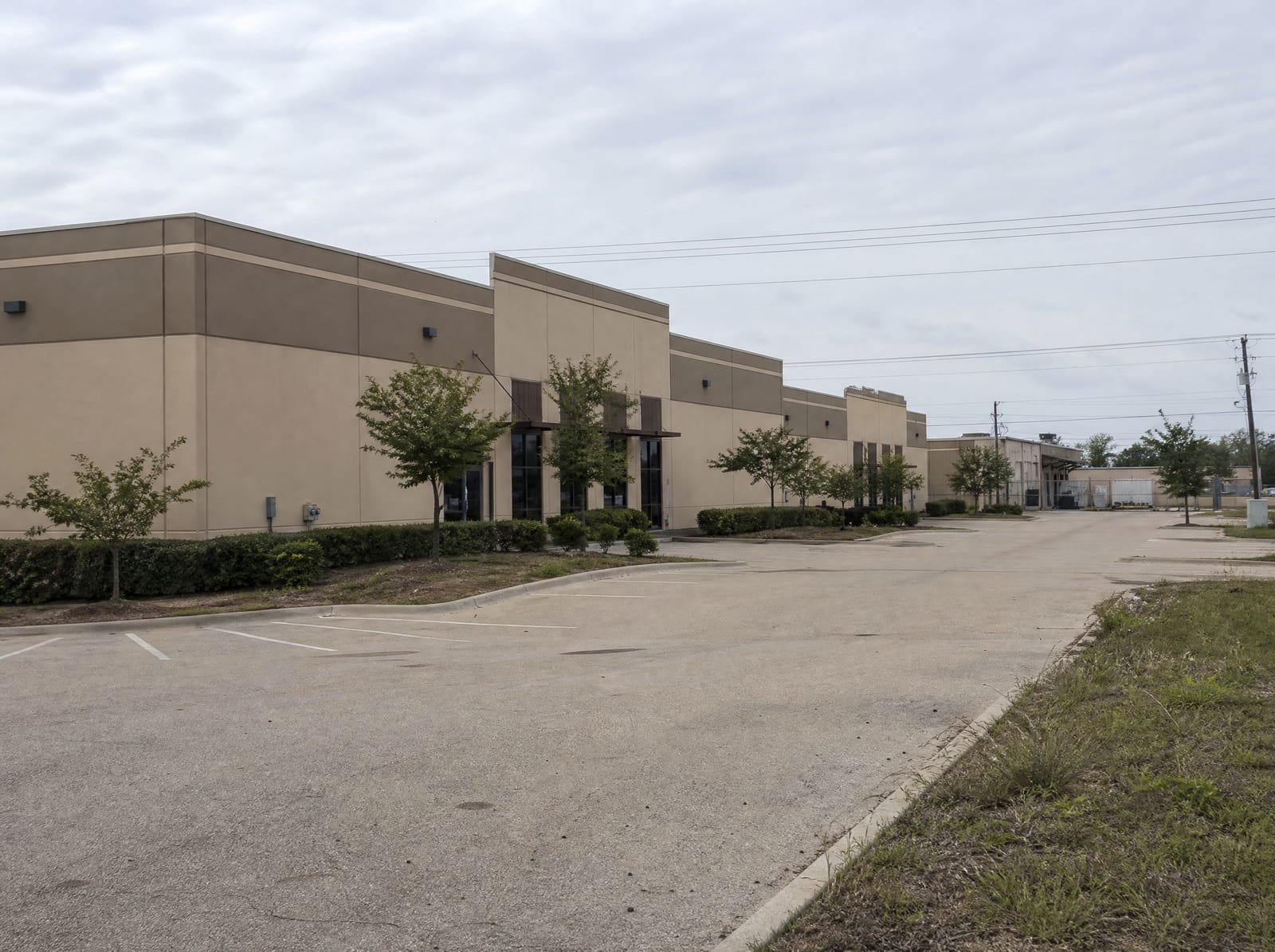 A light-industrial and business-park district in Stafford, Texas, with low tilt-wall warehouse and flex buildings, wide asphalt parking lots, a loading area, and young landscaping under an overcast sky