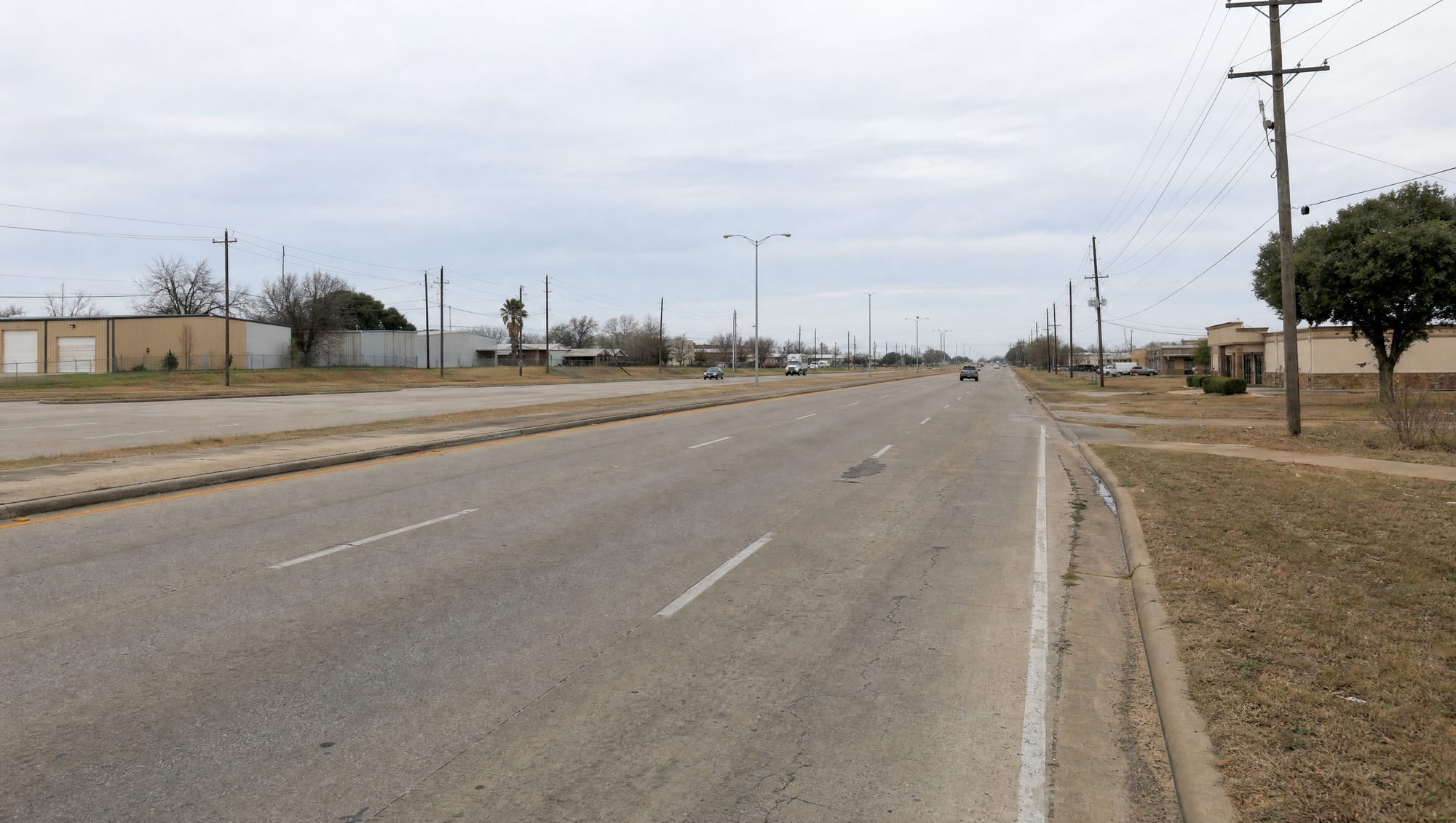 The US-59 and Highway 90A corridor through Stafford, Texas in Fort Bend County, a wide multi-lane road with modest commercial and low light-industrial frontage, utility poles and lines, and flat terrain under a big pale sky