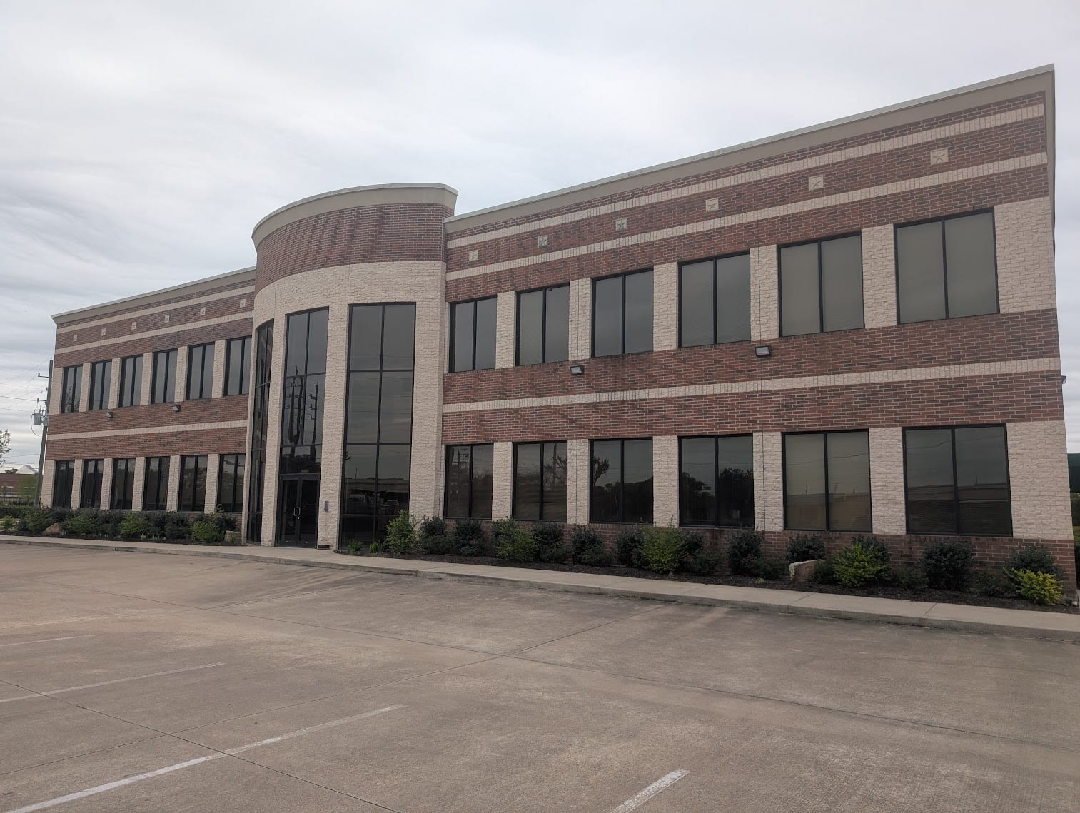 The two-story red-brick and cream-stone Showalter Colgin and Davis office building in Richmond, Texas, with a curved glass entrance tower, under a soft overcast sky